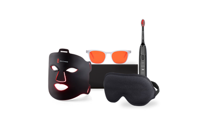 Face mask next to a black sleep mask, blue light blocking glasses with red lenses, and black electric toothbrush.